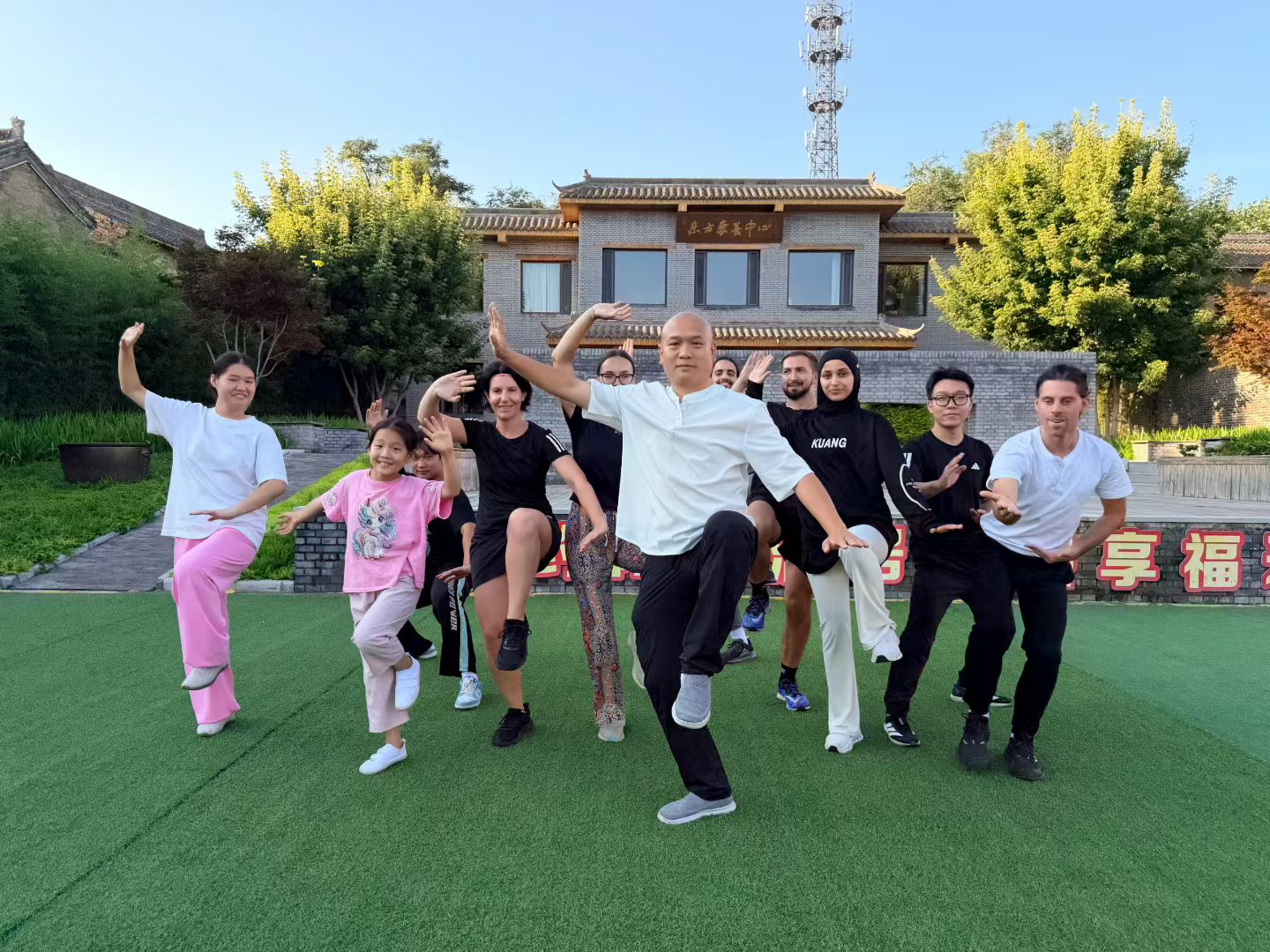 Master Shen and a diverse group of students posing in a dynamic kung fu stance outdoors. Master Shen and a diverse group of students posing in a dynamic kung fu stance outdoors.